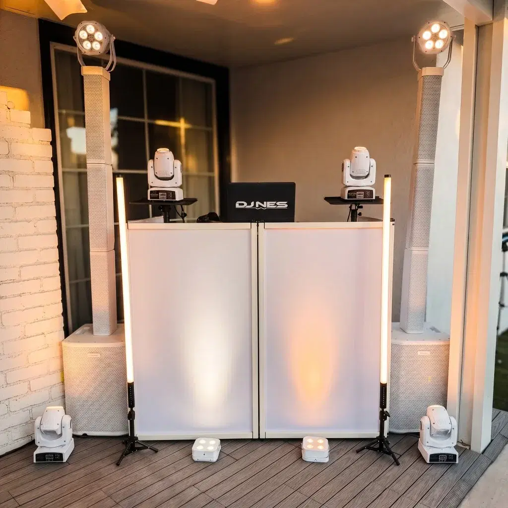 White mobile DJ booth with column speakers, moving-head lights, and LED tubes on a wooden deck for an outdoor birthday event