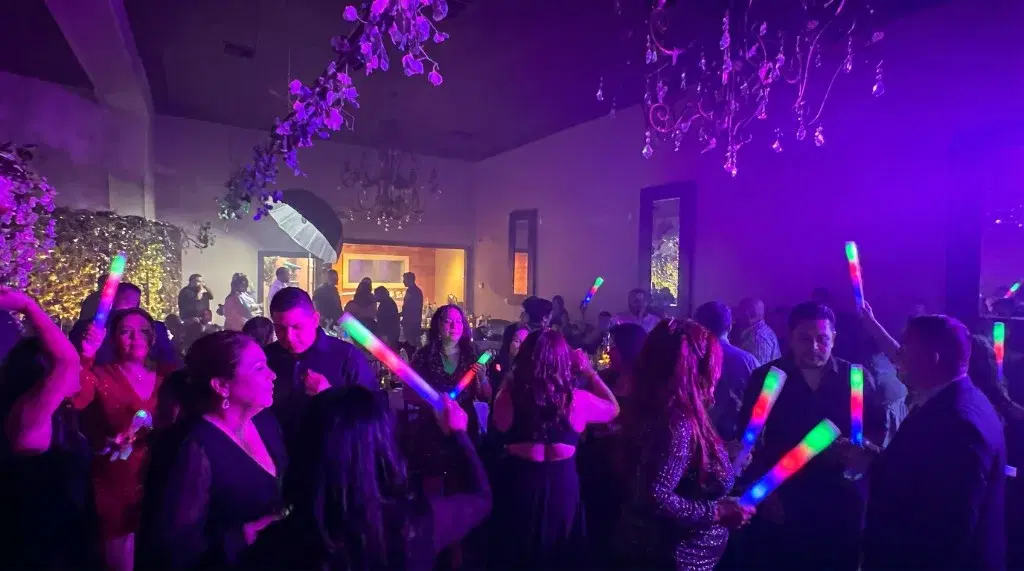 Packed dance floor with guests waving multicolor LED foam sticks under purple and magenta event lighting