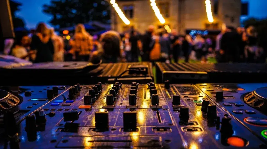 DJ mixer at an outdoor evening party, with string lights over the guests